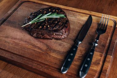 delicious grilled steak with cutlery on wooden board clipart