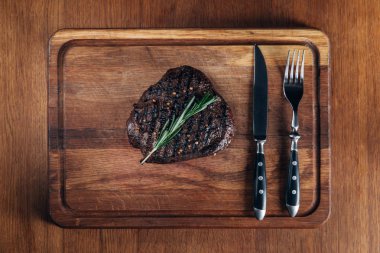 top view of grilled steak with cutlery on wooden board clipart