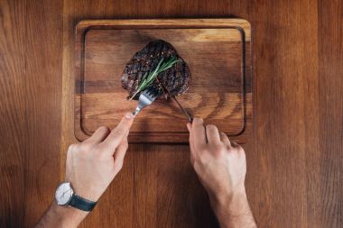 cropped shot of man cutting grilled steak on wooden board clipart