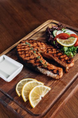 ızgara somon Steak ahşap tahta üzerinde limon dilimleri ve salata ile servis yakın çekim shot