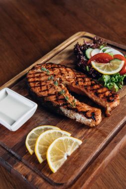 close-up shot of grilled salmon steak served on wooden board with lemon slices and salad clipart