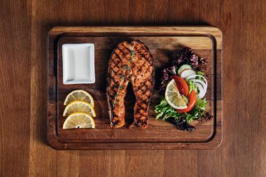 top view of grilled salmon steak served on wooden board with lemon and salad clipart