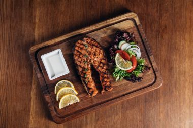 Üstten Görünüm lezzetli ızgara somon Steak ahşap tahta limon dilimleri ve salata ile servis