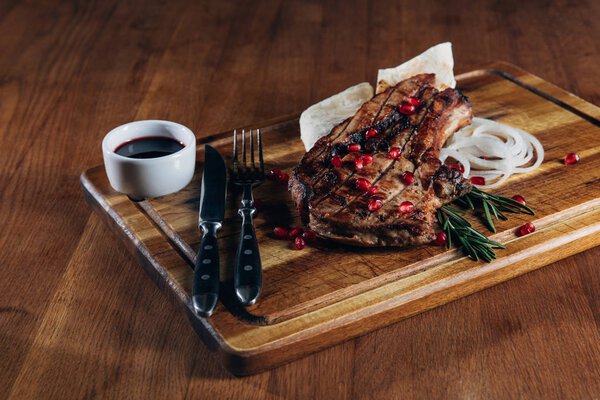 close-up shot of tasty grilled steak served with sauce and pomegranate seeds on wooden board