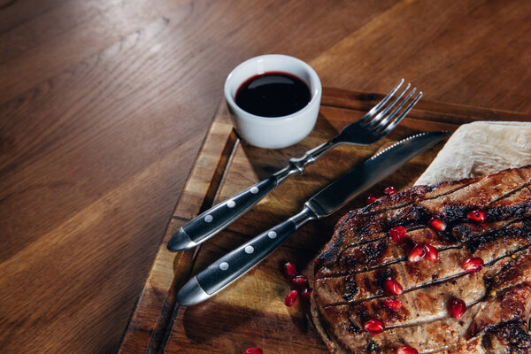 tasty grilled steak served with sauce and pomegranate seeds on wooden board