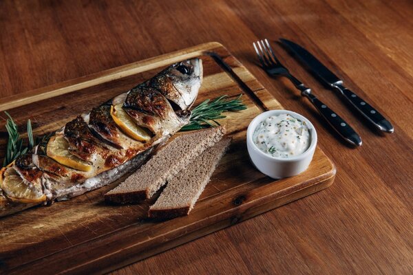 close-up shot of grilled fish with lemon and sauce on wooden board