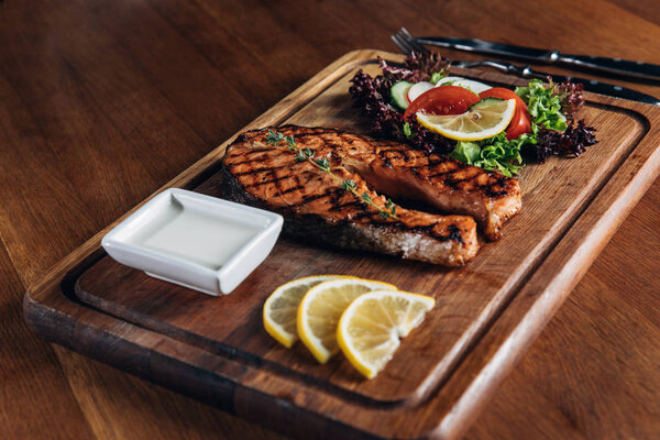 Крупный план вкусный стейк лосося на гриле подается на деревянной доске с лимоном и салатом
