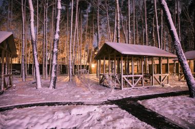territory of wooden cottage in snowy forest in evening clipart