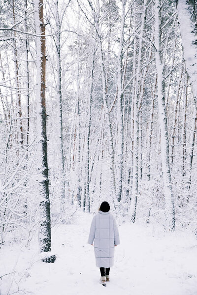 back view of woman walking in snowy forest
