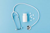 Stethoskop, verstreute Pillen und Packung isoliert auf blauem Hintergrund