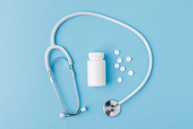 stethoscope, scattered pills and package isolated on blue background clipart