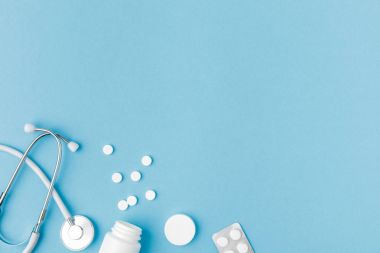 container, scattered pills and stethoscope isolated on blue background    clipart