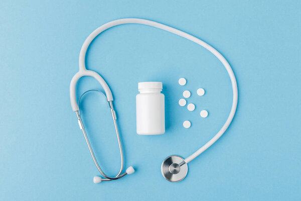 стетоскоп, разбросанные таблетки и упаковка изолированы на синем фоне
