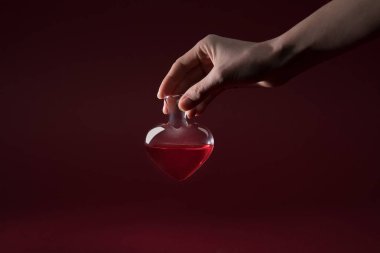 cropped image of woman holding heart shaped glass jar of love potion isolated on red