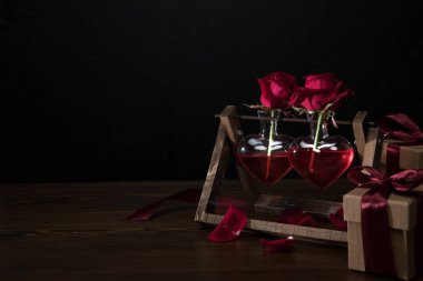 kalbinde iki kırmızı gül vazo ahşap stand ve hediye kutuları şeklinde