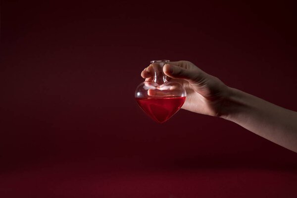 cropped image of woman holding heart shaped glass jar of perfume isolated on red