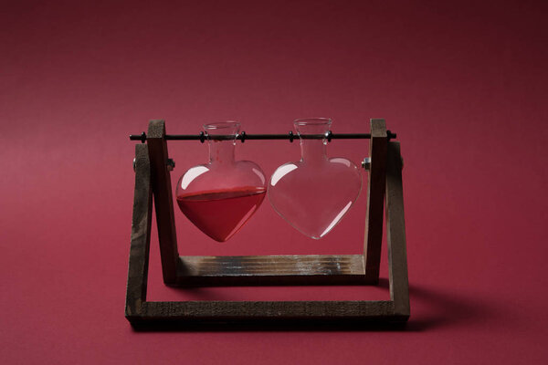 heart shaped glass jar with perfume and empty glass jar on wooden stand on red