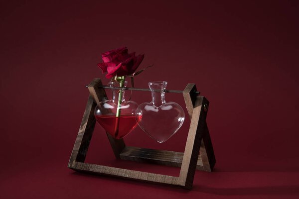 red rose in heart shaped vase and empty vase on wooden stand on red