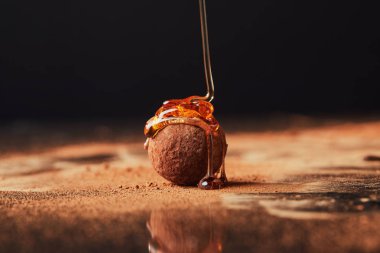 close up view of pouring caramel onto truffle process on black clipart