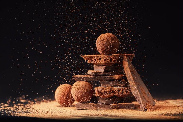 close up view of arrangement of truffles and chocolate bars with cocoa powder on black