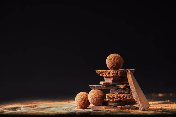 close up view of arrangement of truffles and chocolate bars with cocoa powder on black