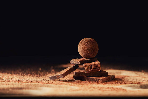 close up view of truffle on chocolate bars with cocoa powder on black