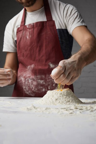 cropped image of chef preparing dough and adding egg to flour