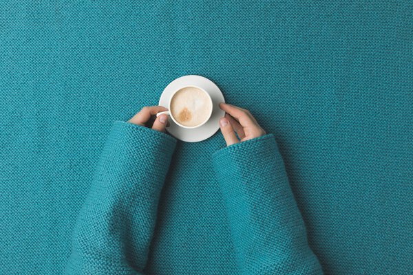 cropped view of woman hands with cup of coffee laying over turquoise fabric 