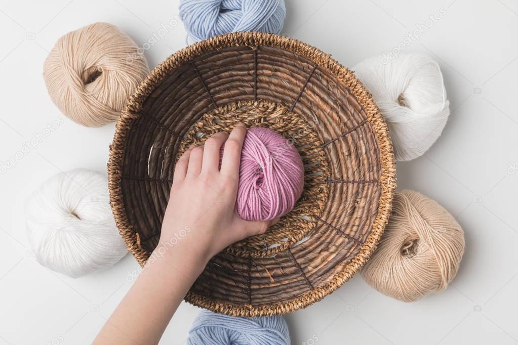 cropped view of woman holding pink yarn ball in hand in wicker basket on white background 