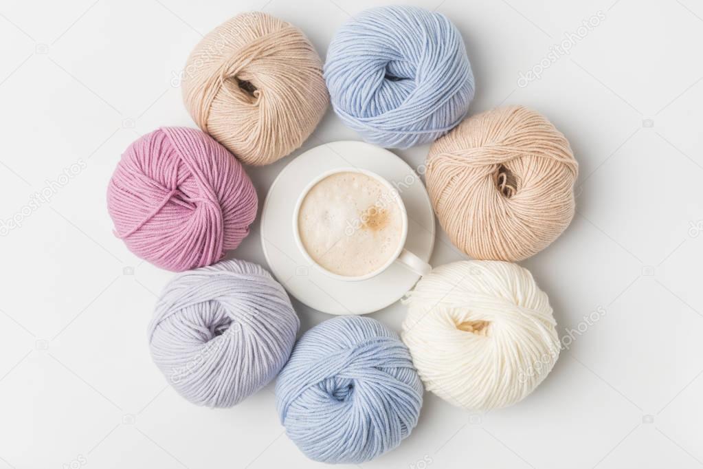 top view of circle of colored yarn balls and coffee in cup on white background  