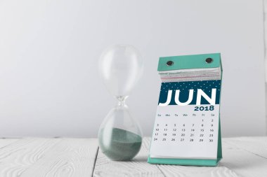 close up view of hourglass and june calendar on wooden tabletop isolated on white clipart