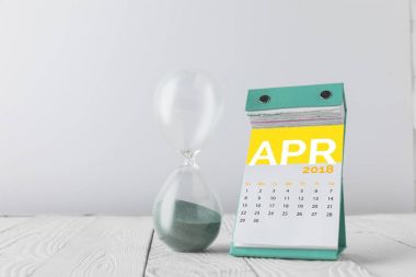 close up view of hourglass and april calendar on wooden tabletop isolated on white clipart