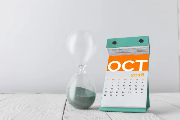 close up view of hourglass and october calendar on wooden tabletop isolated on white