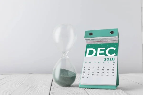 close up view of hourglass and december calendar on wooden tabletop isolated on white