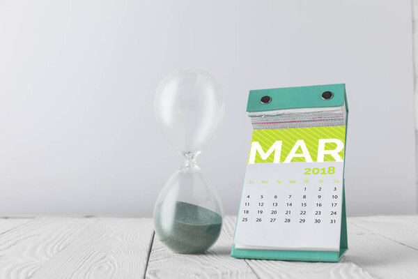 close up view of hourglass and march calendar on wooden tabletop isolated on white