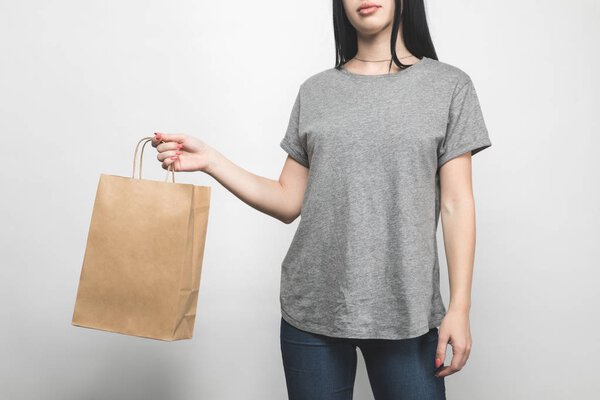cropped shot of young woman in blank grey t-shirt on white with shopping bag