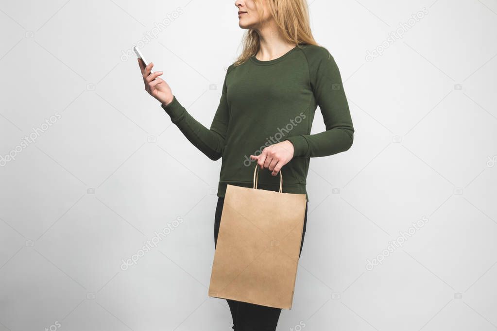 cropped shot of woman in blank green sweatshirt on white with shopping bag and smartphone