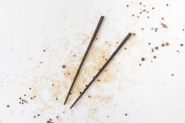 top view of raw rice and spices spilled on white surface with chopsticks clipart