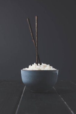 bowl of freshly cooked rice with chopsticks on black table clipart