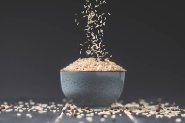 side view of rice spilling into bowl on black table clipart