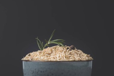 close-up shot of bowl of raw rice with rosemary and spices on black surface clipart
