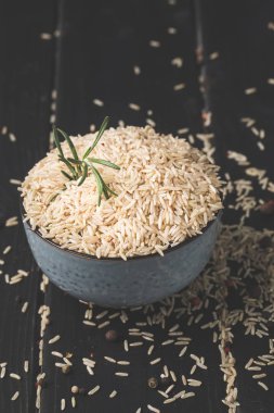 close-up shot of bowl of raw rice with rosemary on black surface clipart