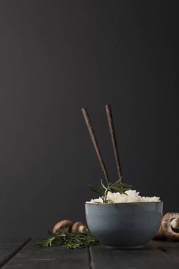 bowl of tasty rice with chopsticks and mushrooms on black tabletop clipart