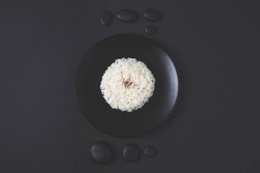 top view of tasty rice on plate with pebbles on black table clipart