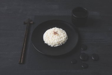 rice with cup of tea and chopsticks on black table clipart