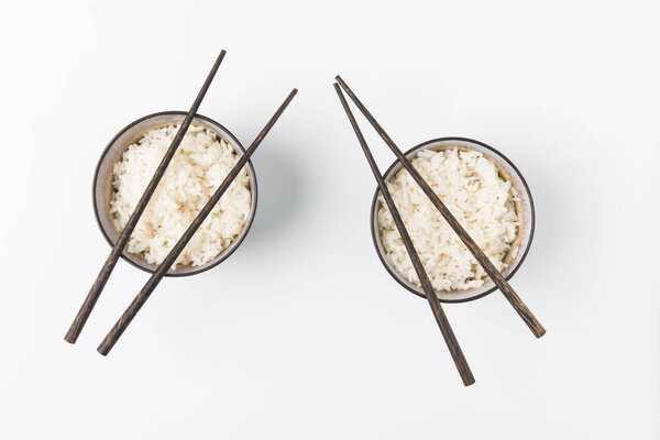 вид сверху на миски вкусного риса с палочками для еды, изолированными на белом
