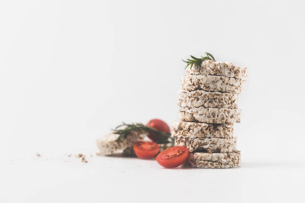 stack of rice cakes with rosemary and tomatoes on white surface