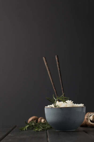 миска вкусного риса с палочками и грибами на черном столе
