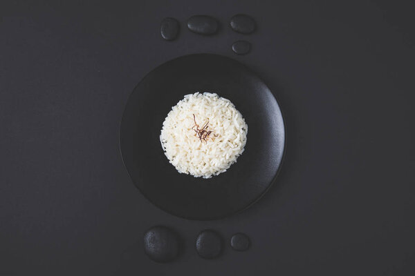 вид сверху на вкусный рис на тарелке с галькой на черном столе
