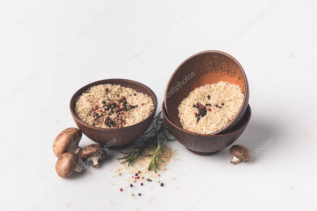 bowls of raw rice with spices and mushrooms on white surface